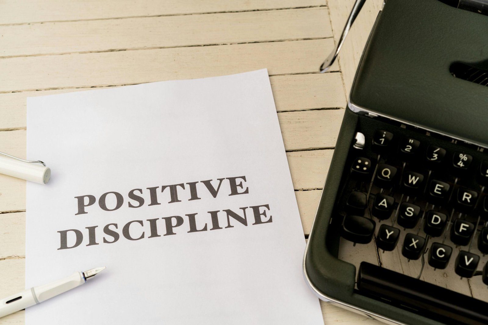 A white sheet of paper with the words “Positive Discipline” printed on it, placed on a light wooden desk beside a vintage typewriter and a pen, symbolizing self improvement and disciplined habits