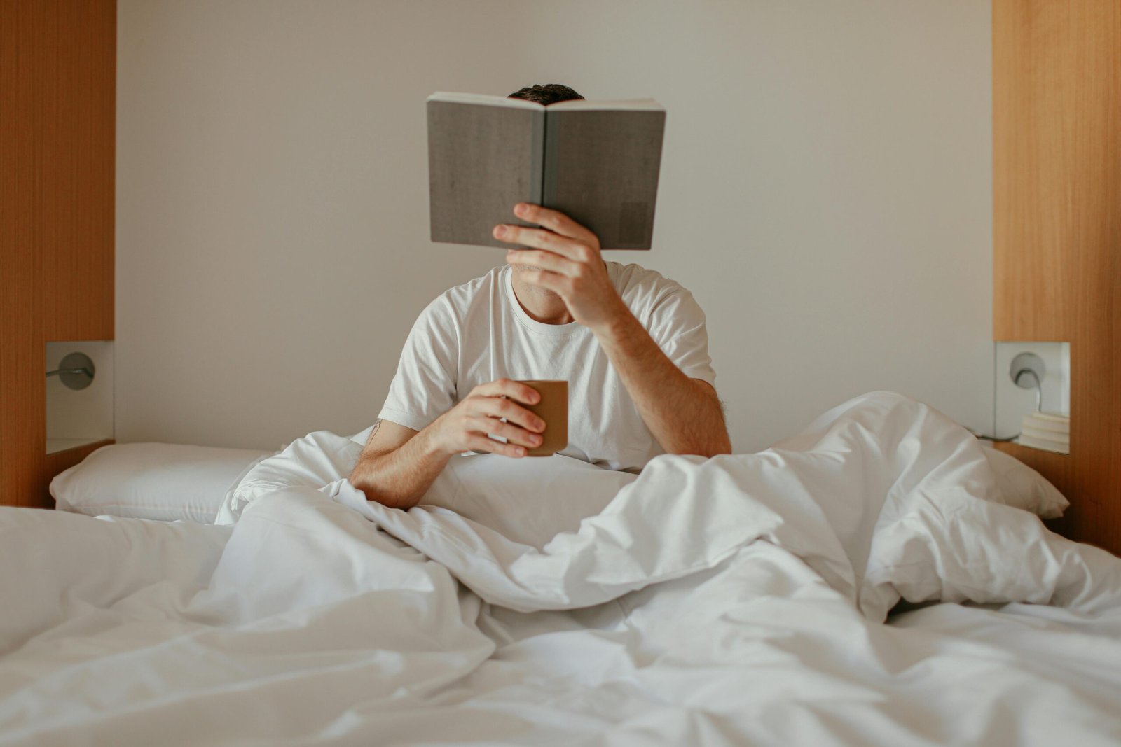Person sitting in bed holding a book and coffee, representing the slow and challenging start of self-improvement habits.